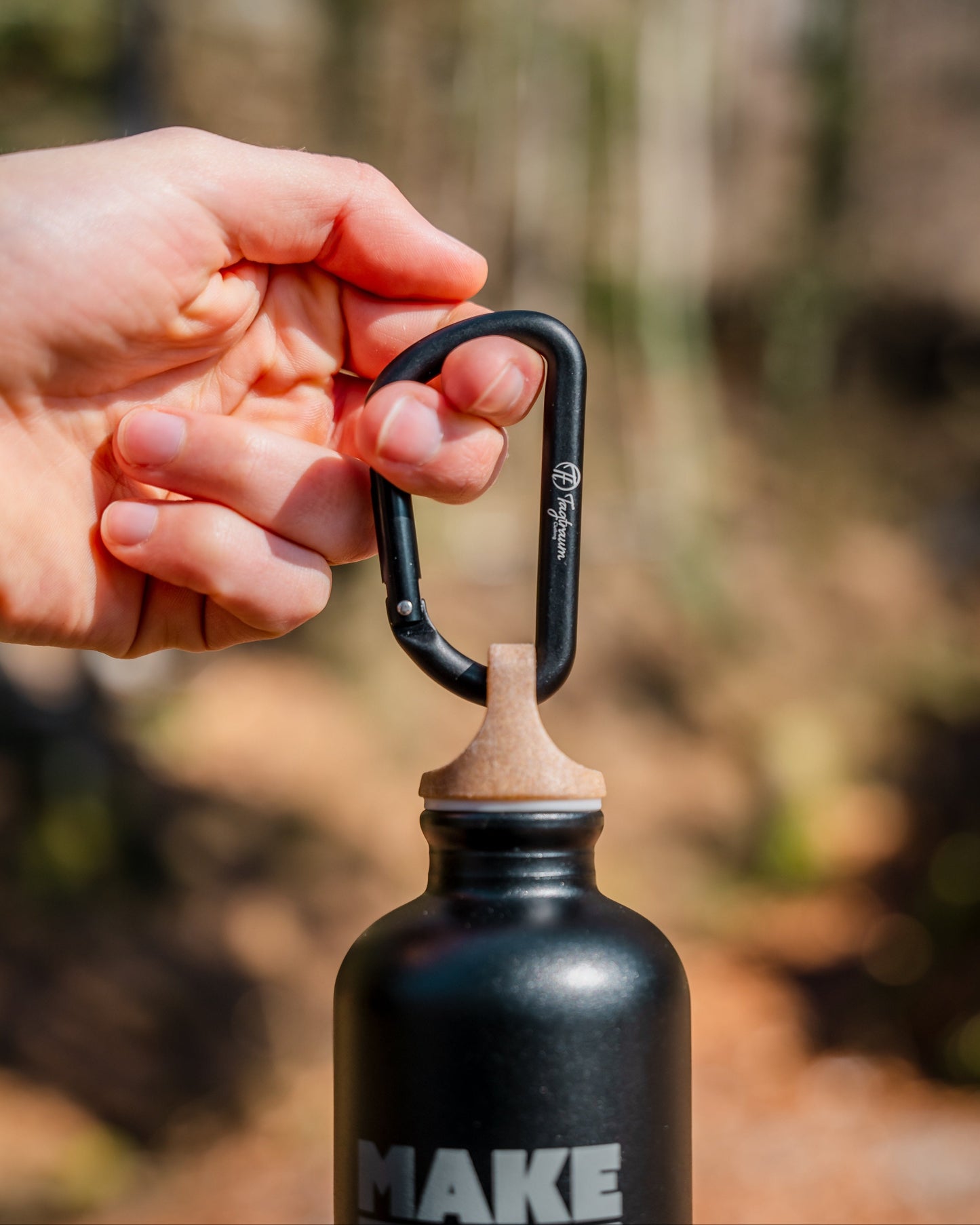 Ein kleiner, schwarzer Aluminium Karabiner, an dem eine Tagtraum Trinkflasche hängt