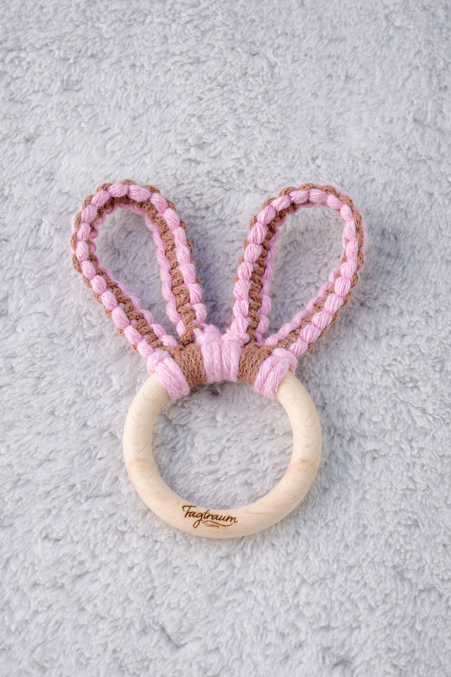 Süsser Hasenohren Greifling für Babys. Aus einem schönen, schadstofffreien Holzring mit edler Tagtraum Gravur und süssen Hasenöhrchen, geknüpft aus Makramee Garn in Rosa und Braun. Handgefertigt von Tagtraum Clothing in der Schweiz