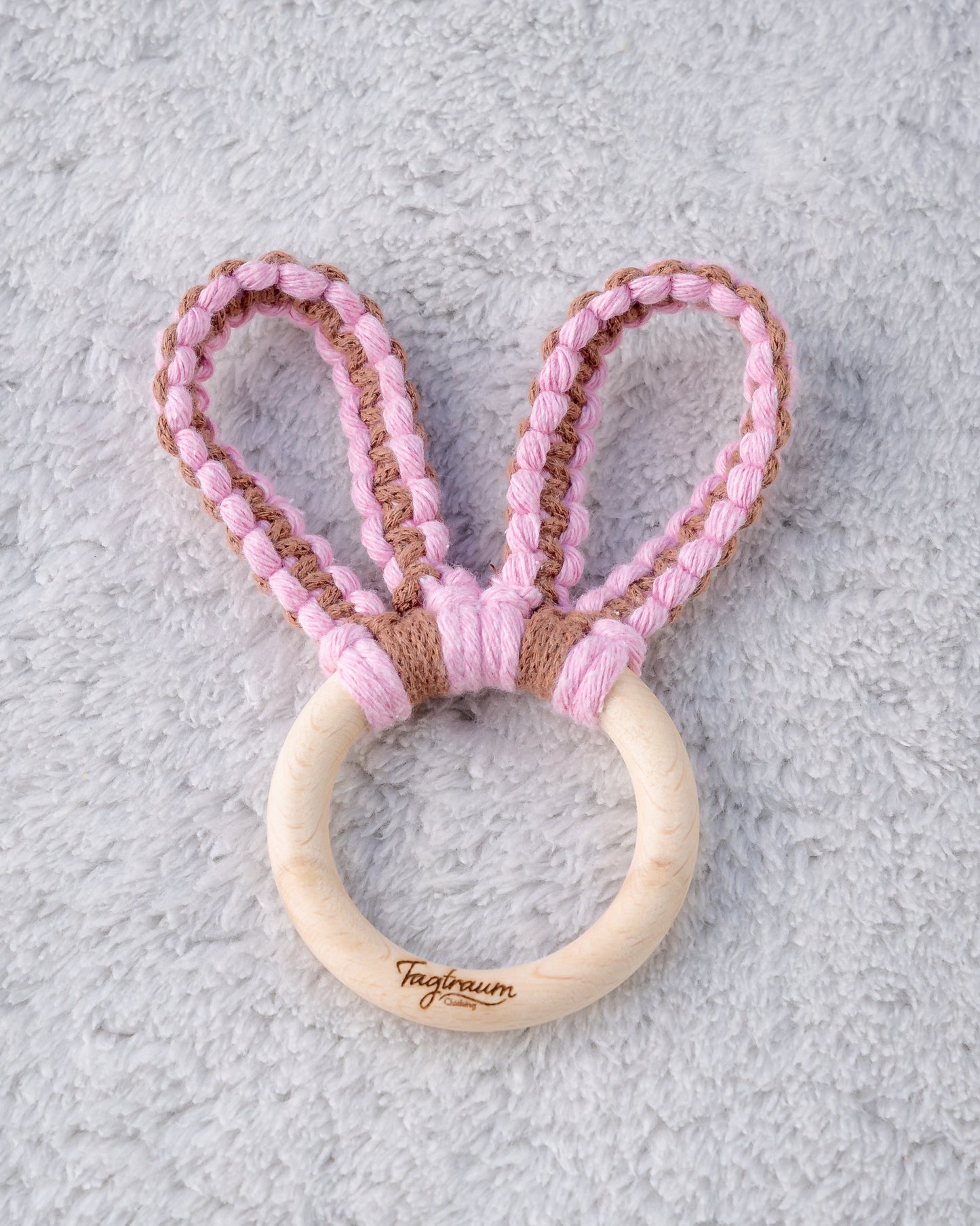 Süsser Hasenohren Greifling für Babys. Aus einem schönen, schadstofffreien Holzring mit edler Tagtraum Gravur und süssen Hasenöhrchen, geknüpft aus Makramee Garn in Rosa und Braun. Handgefertigt von Tagtraum Clothing in der Schweiz