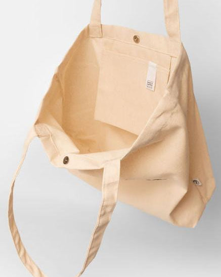 eine naturfarbene Bio-Baumwolltasche. Zu sehen ist die Innenseite des Shoppers, mit der praktischen Innentasche, der "Make it happen"-Lasche für den Schlüsselbund o.ä., sowie dem Druckknopf