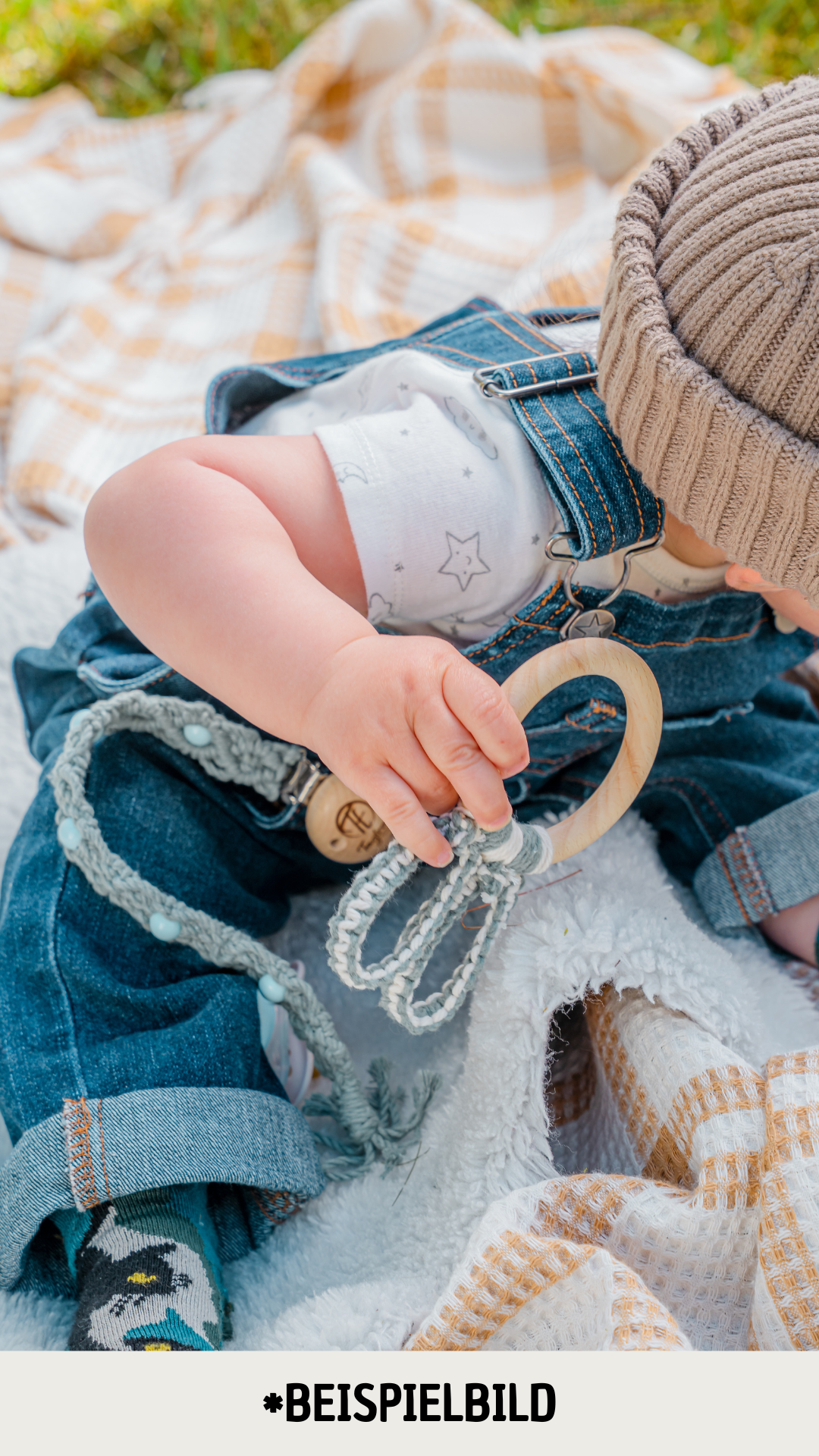 Ein Baby hält einen süssen Hasenohren Beissring in der Hand und sitzt draussen auf einer Pick-Nick Decke, das Gesicht ist nicht zu sehen. Der Beissring ist aus nachhaltigen, umweltfreundlichen Materialien gefertigt und passt perfekt in kleine Baby-Hände. Zudem ist er aus natürlichen Materialien und komplett Schadstofffrei. Handgefertigt in der Schweiz.