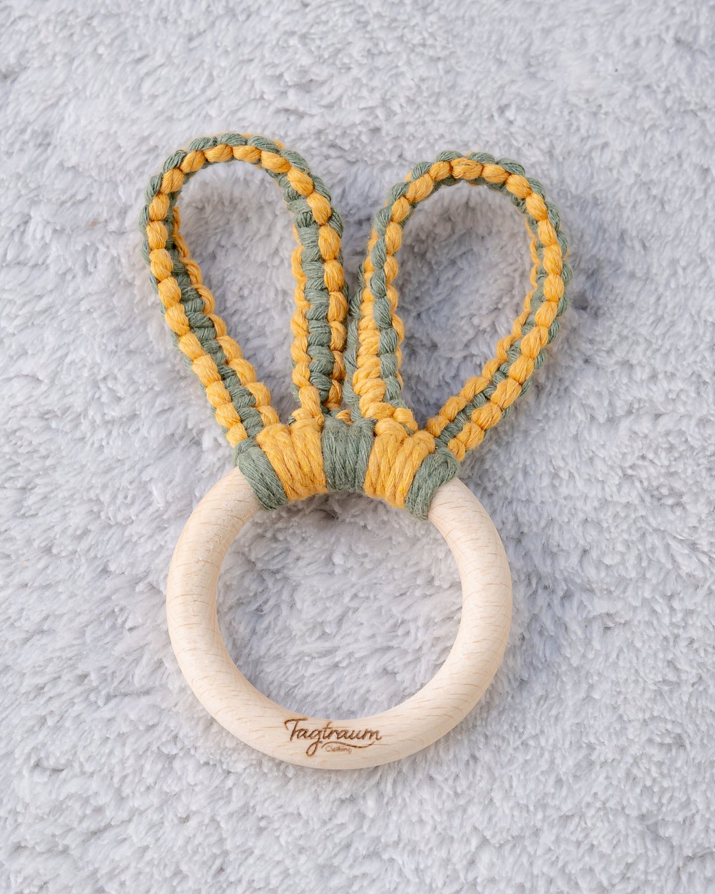 Greifling mit Hasenohren für Babys, aus einem schönen Holzring mit edler Tagtraum Gravur und süssen Hasenöhrchen geknüpft aus Makramee Garn in Eukalyptus Grün und Gelb. Handgefertigt in der Schweiz von Tagtraum Clothing. Frei von Schadstoffen und umweltfreundlich.