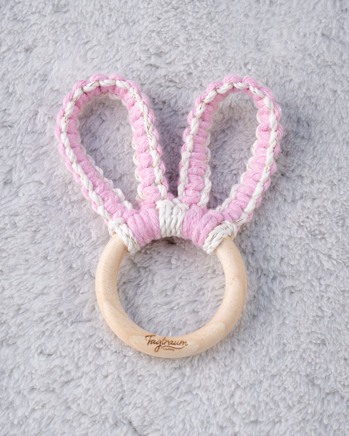 Greifling mit süssen Hasenohren geknüpft aus Makramee Garn in Rosa und Ecru mit Goldeinschlüssen. Der angenehme Holzring ist mit einer edlen Tagtraum Gravus versehen und liegt perfekt in kleinen Babyhändchen. Der Greifling wurde handgefertigt von Tagtraum Clothing in der Schweiz.