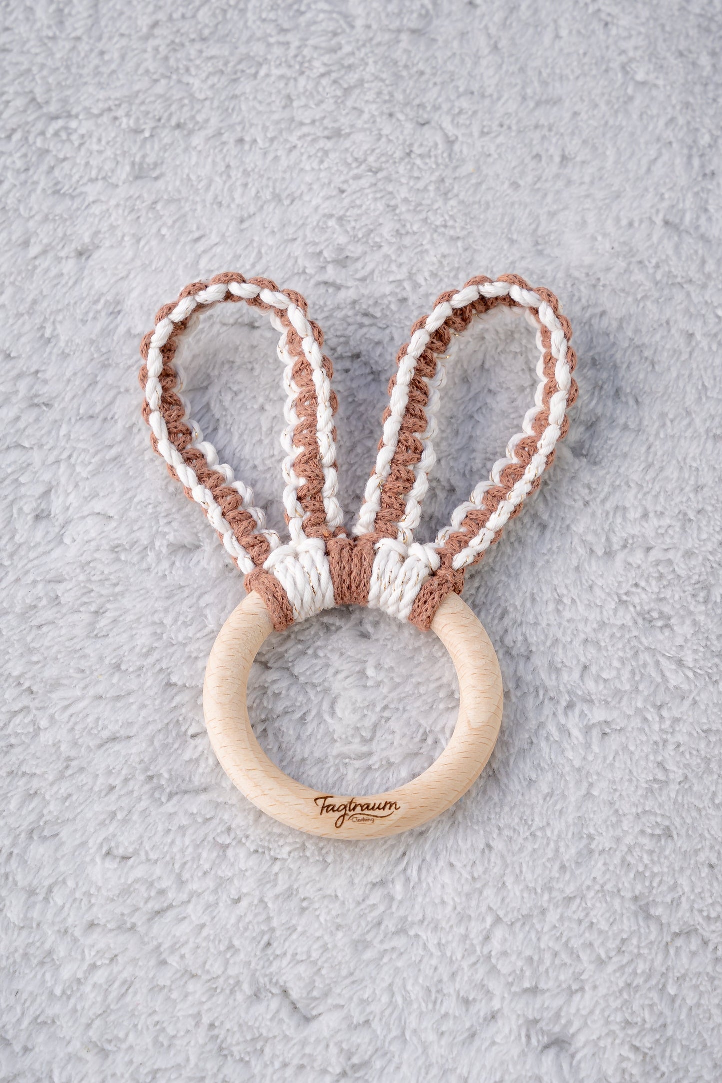 Süsser Greifling für Babies mit Hasenohren aus Makramee Garn, handgefertigt von Tagtraum Clothing. Die Ohren sind aus braunem und eierschalenfarbenem Garn (veredelt mit Goldfäden). Auf dem Holzring befindet sich unsere edle Tagtraum Clothing Gravur.