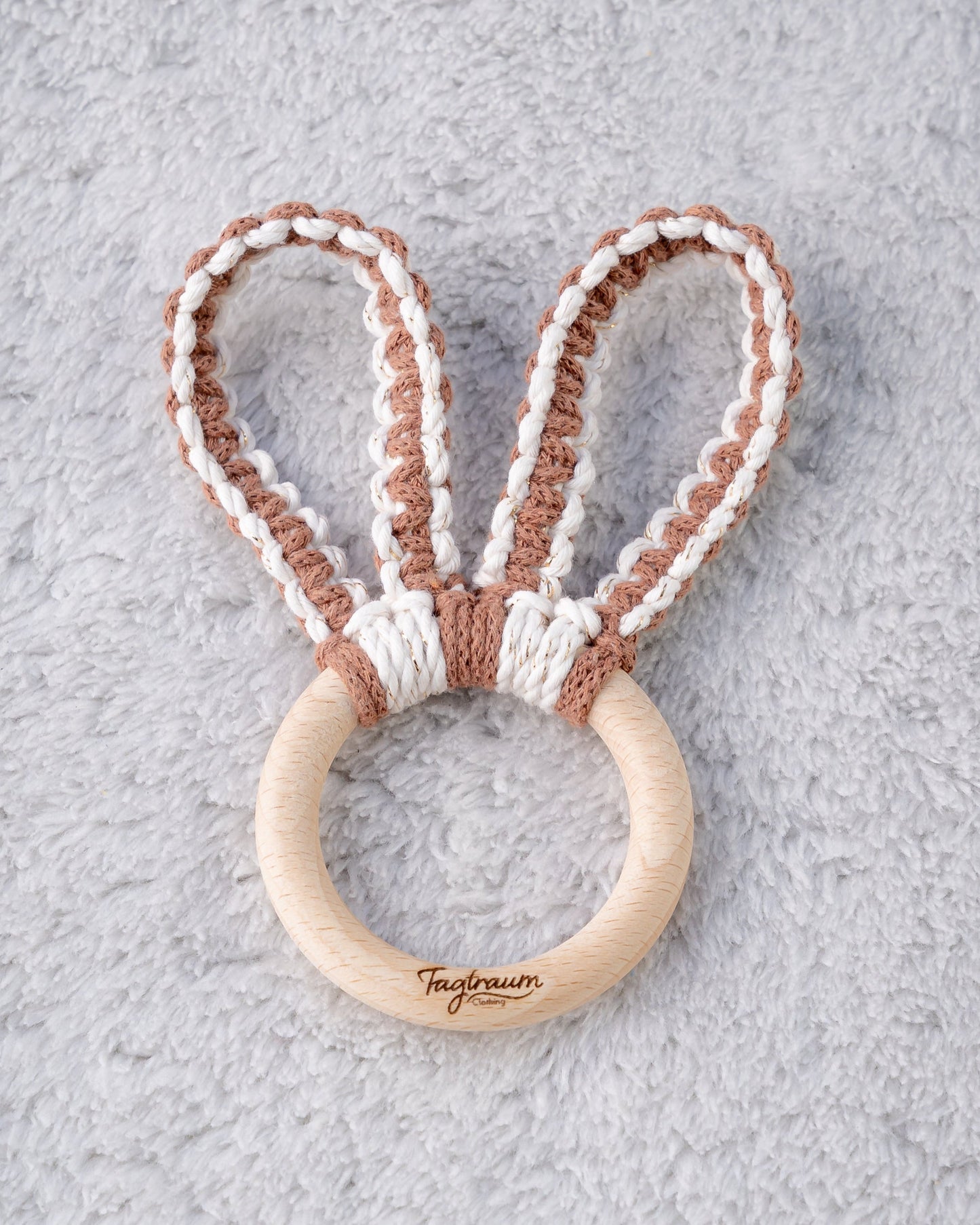 Süsser Greifling für Babies mit Hasenohren aus Makramee Garn, handgefertigt von Tagtraum Clothing. Die Ohren sind aus braunem und eierschalenfarbenem Garn (veredelt mit Goldfäden). Auf dem Holzring befindet sich unsere edle Tagtraum Clothing Gravur.