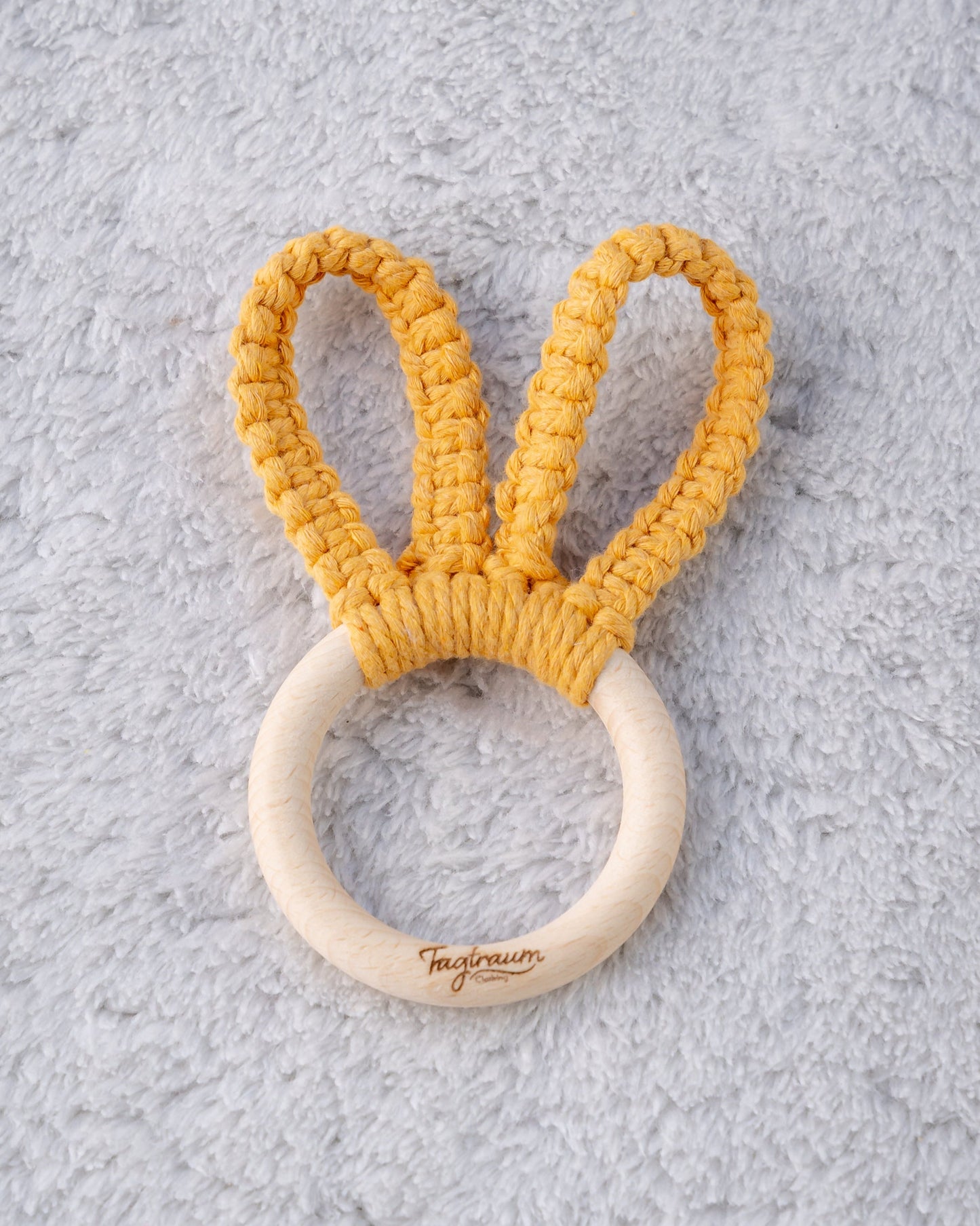 Süsser Greifling für Babys aus einem schönen Holzring mit edler Tagtraum Gravur und süssen Hasenohren, geknüpft aus Makramee Garn in sonnigem Gelb. Frei von Schadstoffen und aus umweltfreundlichen Materialien; handgefertigt in der Schweiz von Tagtraum Clothing.