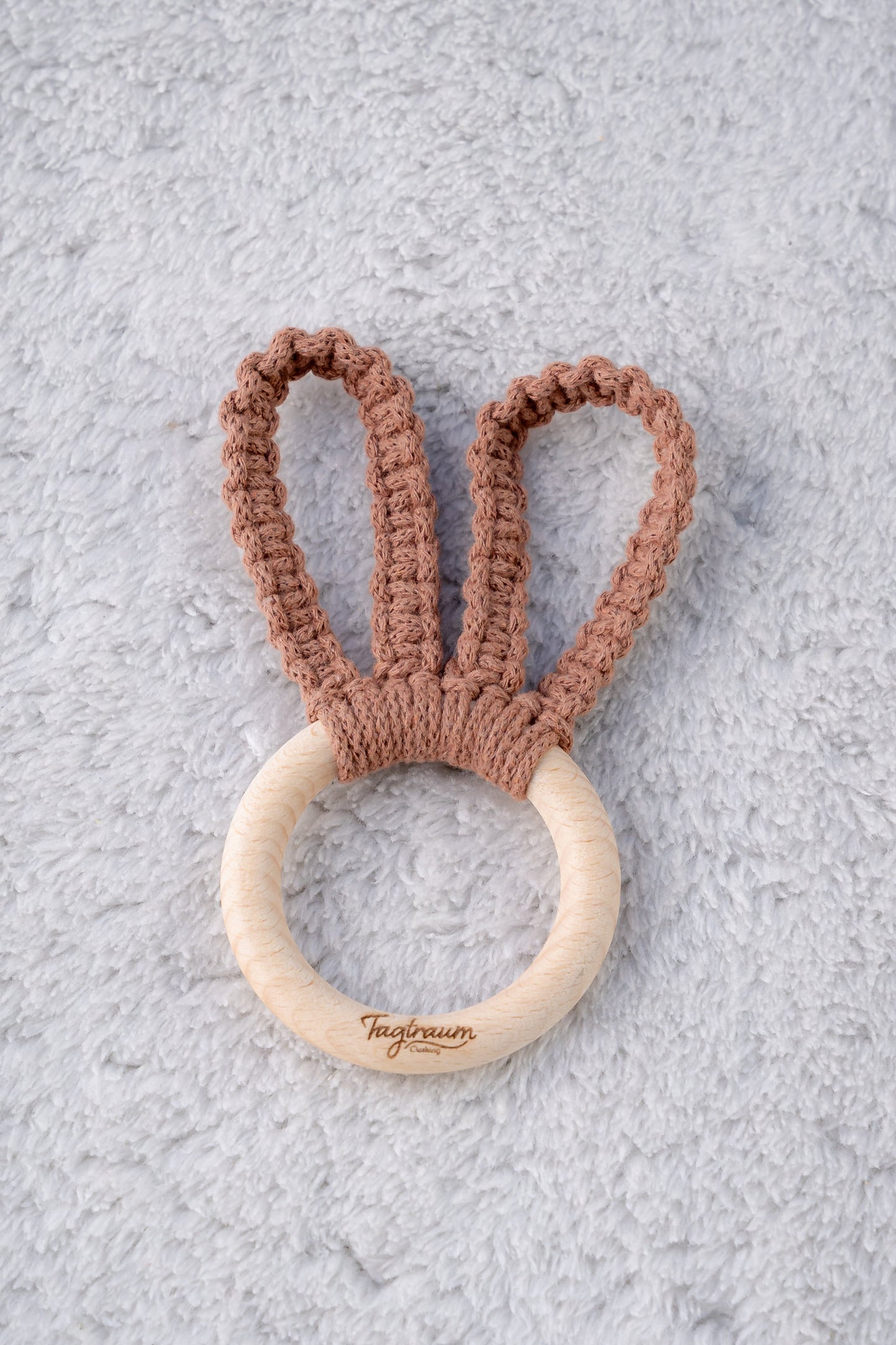 Süsser Hasenohren Greifling für Babys, aus einem schönen Holzring mit edler Tagtraum Gravur und geknüpften Hasenohren aus Makramee Garn in schönem Braun. Handgefertigt in der Schweiz von Tagtraum Clothing; schadstofffrei und umweltfreundlich.
