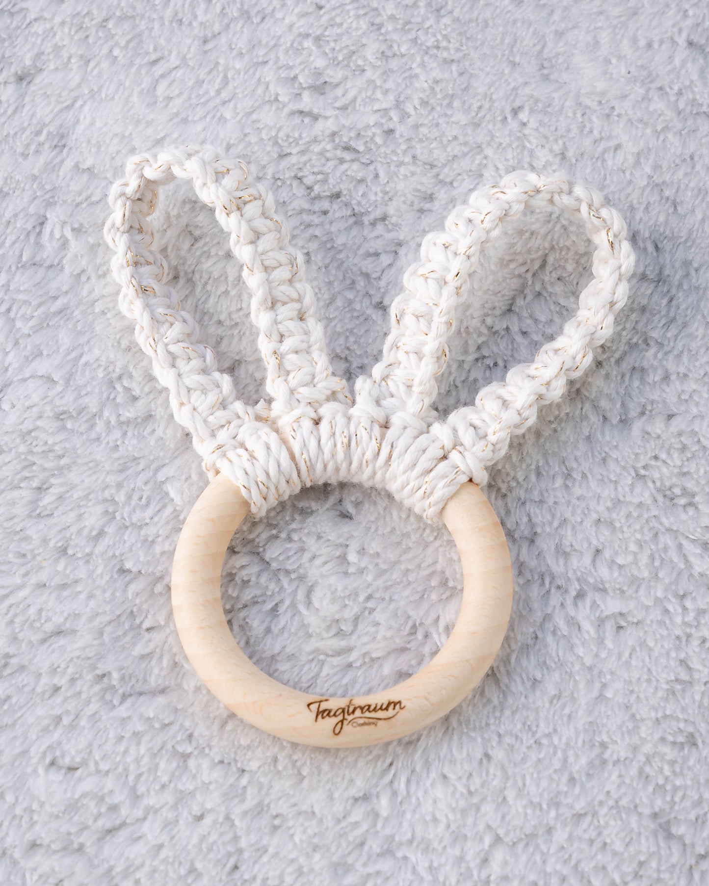 Süsses Hasenohren Greifling für Babys, mit geknüpften Hasenöhrchen aus edlem Garn in Ecru mit Gold. Auf dem angenehmen Holzring befindet sich eine dezente Tagtraum Gravur.