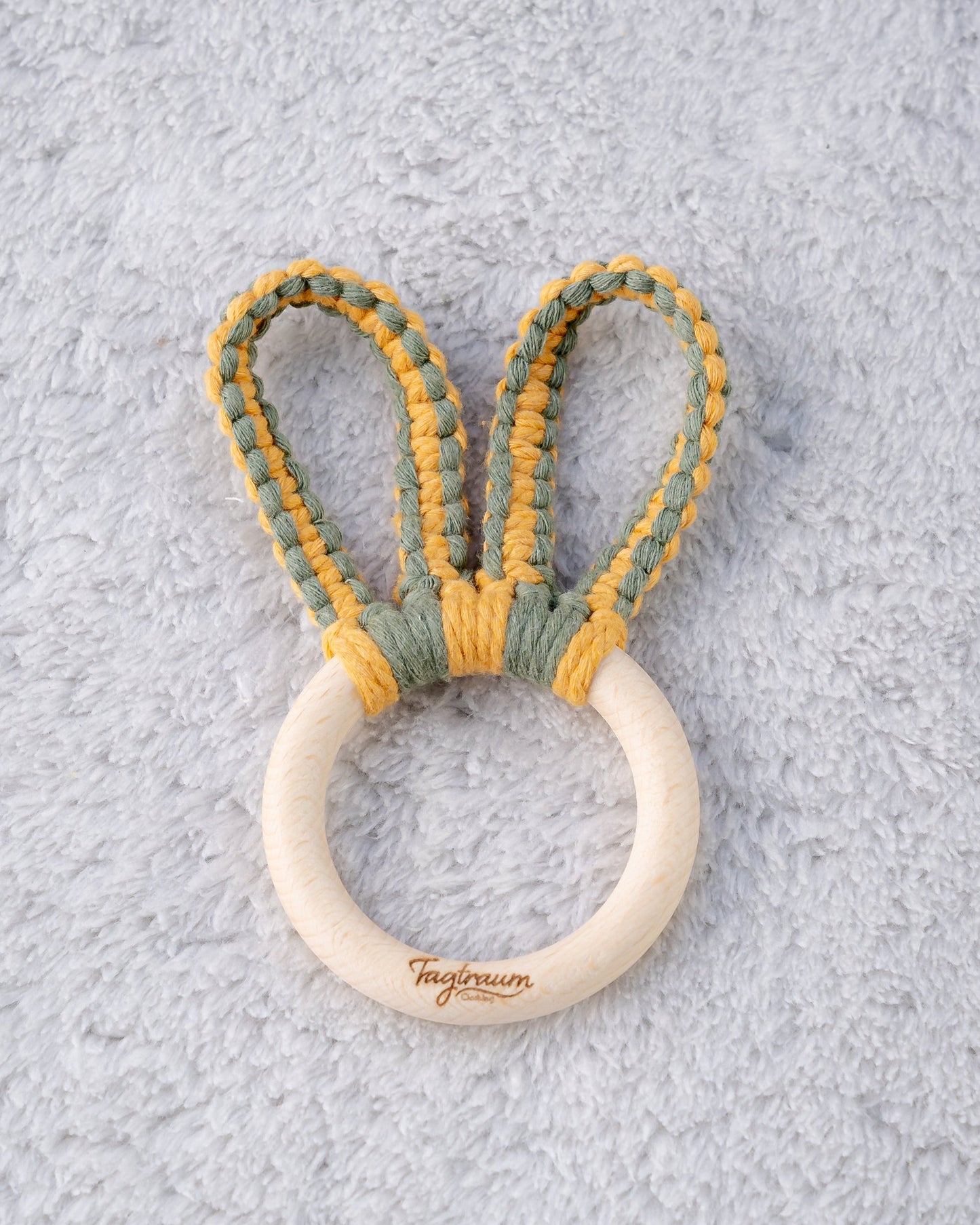 Ein süsser Greifling für Babys mit einem angenehmen Holzring mit edler Tagtraum Gravur und Hasenohren geknüpft aus Makrameegarn in Grün und Gelb. Handgefertigt von Tagtraum Clothing in der Schweiz