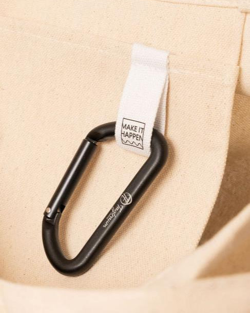 Der kleine Aluminium Karabiner an der "Make it happen"-Lasche im Bio-Baumwoll Shopper befestigt