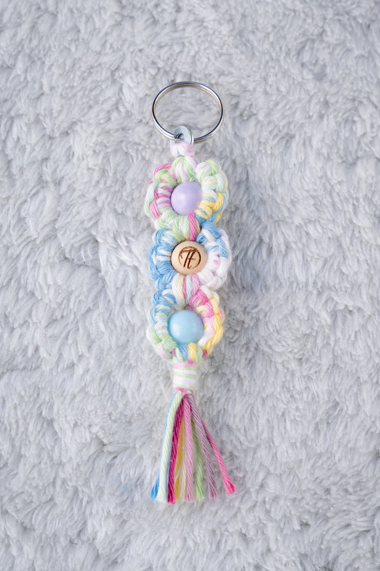 Schöner Makramee Schlüsselanhänger geknüpft aus buntem, farbenfrohem Garn, mit drei Holzperlen, eine davon versehen mit unserem Tagtraum Logo, die anderen Lila und Babyblau. Umweltfreundlich, nachhaltig und handgefertigt von uns in der Schweiz.