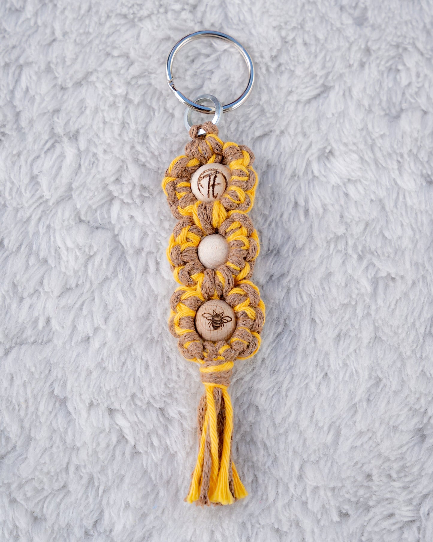 Schöner Makramee Schlüsselanhänger geknüpft aus einem gelb-braunem Garnmix, mit drei naturfarbenen Holzperlen, eine davon versehen mit unserem Tagtraum Logo, die andere mit einem süssen Bienchen, eine unifarben natur. Umweltfreundlich, nachhaltig und handgefertigt von uns in der Schweiz.