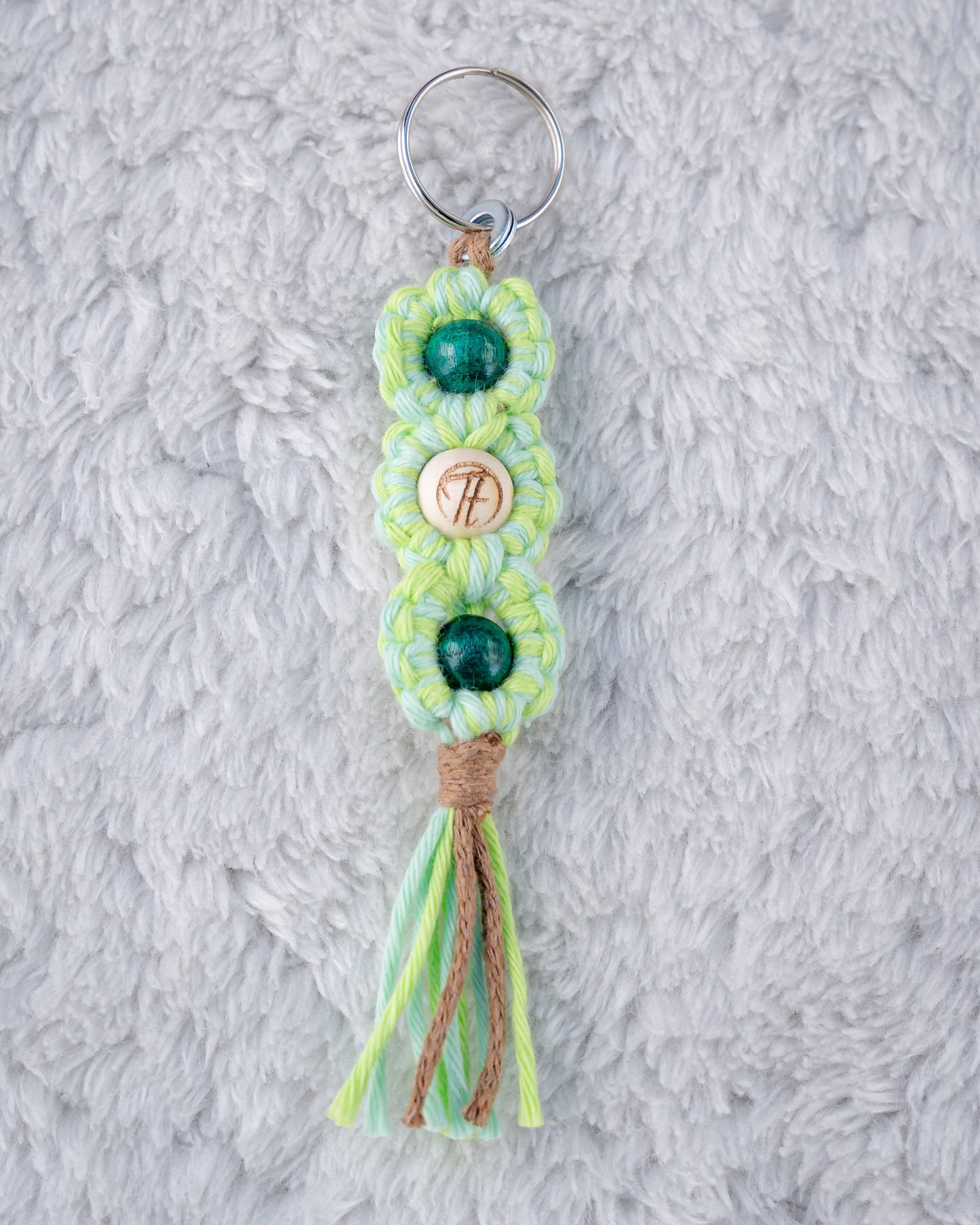 Schöner Makramee Schlüsselanhänger geknüpft aus einem grün/braunem Garnmix, mit drei Holzperlen, eine davon versehen mit unserem Tagtraum Logo, die anderen in einem dunklen Grün Pink. Umweltfreundlich, nachhaltig und handgefertigt von uns in der Schweiz.