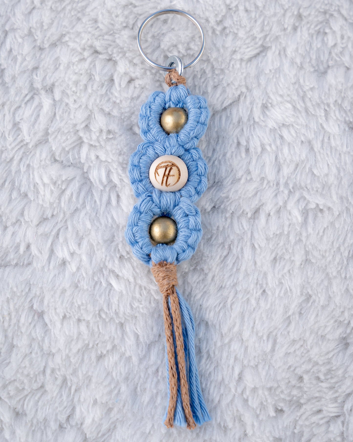 Schöner Makramee Schlüsselanhänger geknüpft aus blauem und braunem Garnmix, mit drei Holzperlen, eine davon versehen mit unserem Tagtraum Logo, die anderen Gold. Umweltfreundlich, nachhaltig und handgefertigt von uns in der Schweiz.