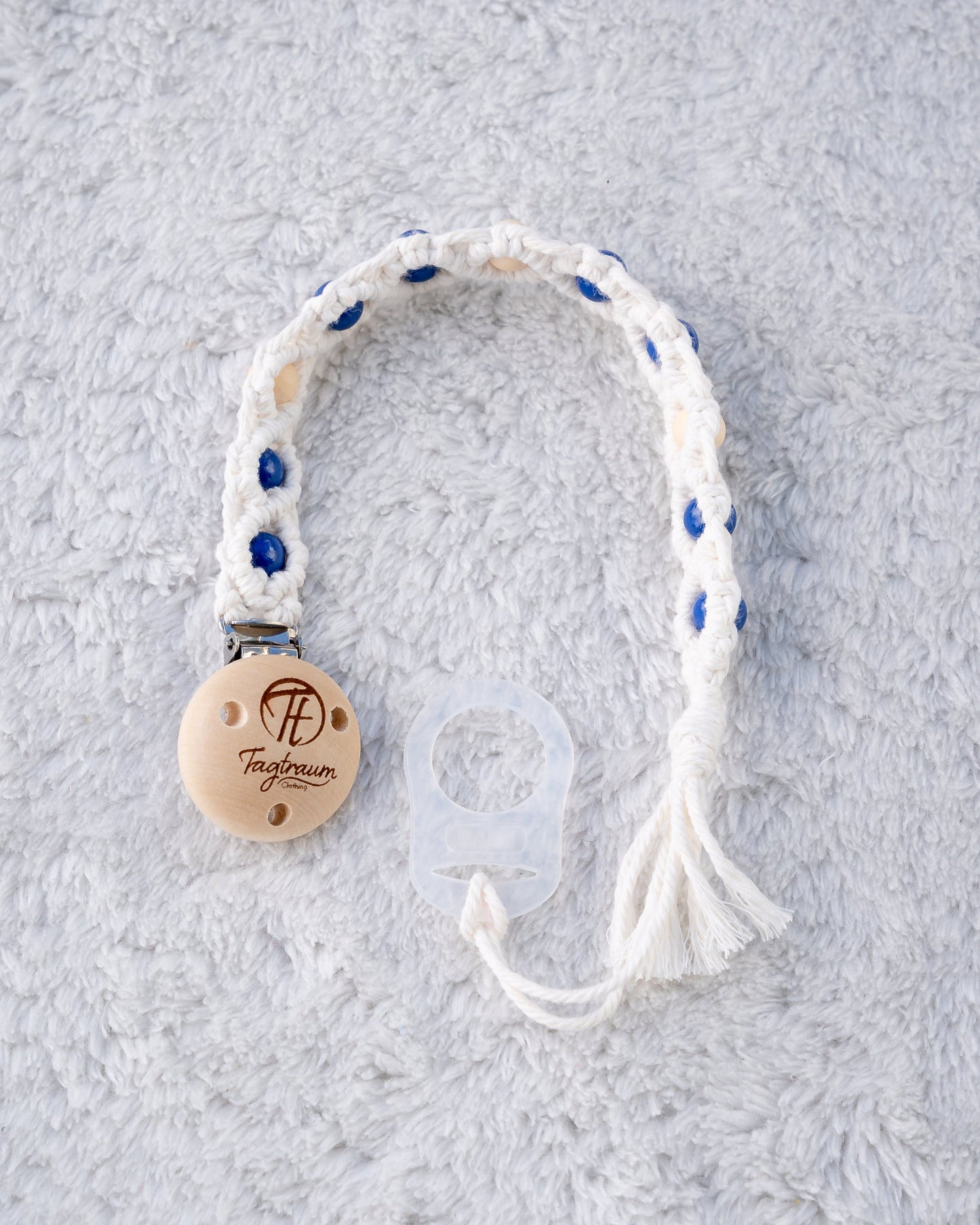 Schöne Schnullerkette aus offwhite Garn mit dunkelblauen und naturfarbenen Holzperlen, einem hochwertigen Schnullerclip aus Holz, und einem Adapter für MAM Schnuller. Auf dem Holzclip befindet sich eine dle Tagtraum Cothing Gravur mit Logo. Die Schnullerketten werden handgefertigt von Tagtraum Clothing in der Schweiz.