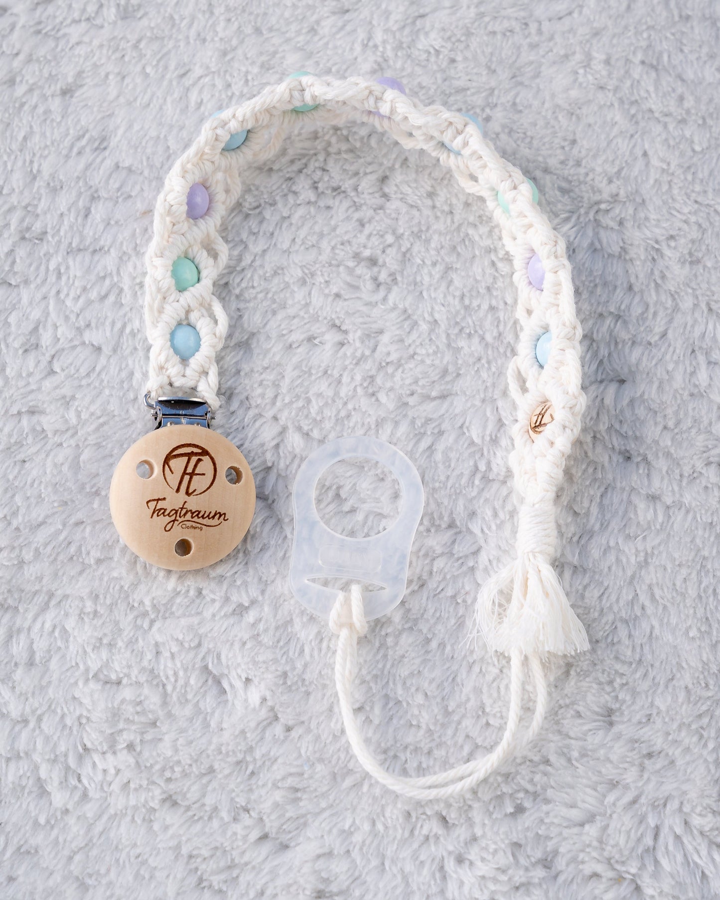 Schöne Schnullerkette aus weissem Garn mit babyblauen,türkisen und lila Holzperlen, einem hochwertigen Schnullerclip aus Holz, und einem Adapter für MAM Schnuller. Auf dem Holzclip befindet sich eine dle Tagtraum Cothing Gravur mit Logo. Die Schnullerketten werden handgefertigt von Tagtraum Clothing in der Schweiz.