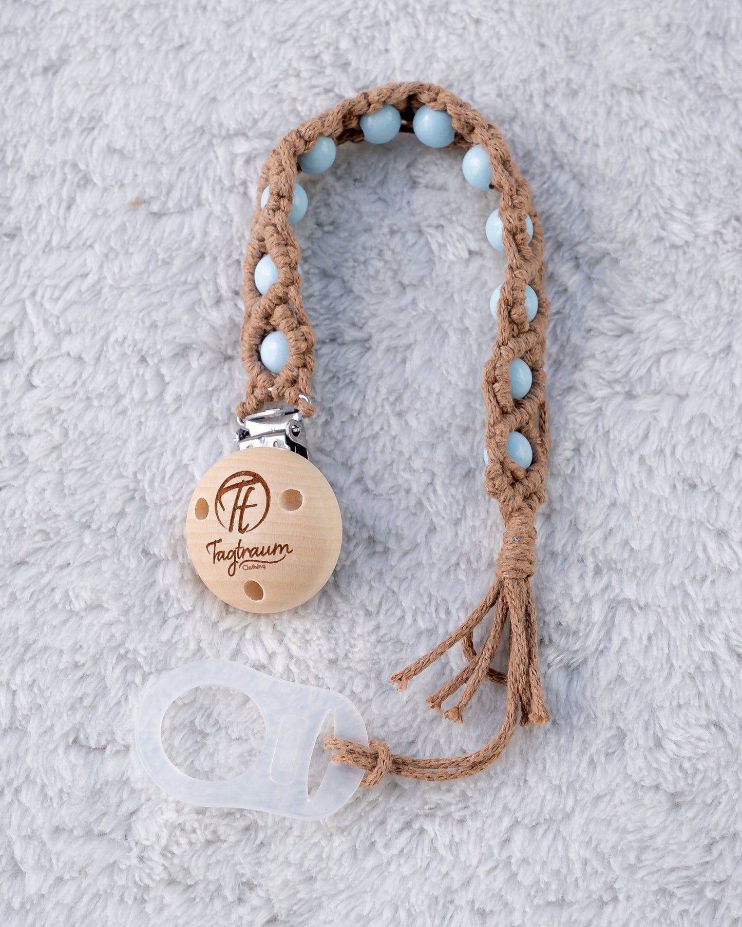 Schöne Schnullerkette aus braunem Garn mit babyblauen Holzperlen, einem hochwertigen Schnullerclip aus Holz, und einem Adapter für MAM Schnuller. Auf dem Holzclip befindet sich eine dle Tagtraum Cothing Gravur mit Logo. Die Schnullerketten werden handgefertigt von Tagtraum Clothing in der Schweiz.