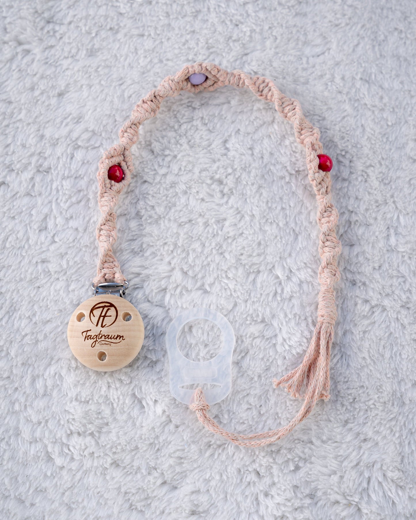 Schöne Schnullerkette aus lachsrosanem Garn mit pinken und lila Holzperlen, einem hochwertigen Schnullerclip aus Holz, und einem Adapter für MAM Schnuller. Auf dem Holzclip befindet sich eine dle Tagtraum Cothing Gravur mit Logo. Die Schnullerketten werden handgefertigt von Tagtraum Clothing in der Schweiz.