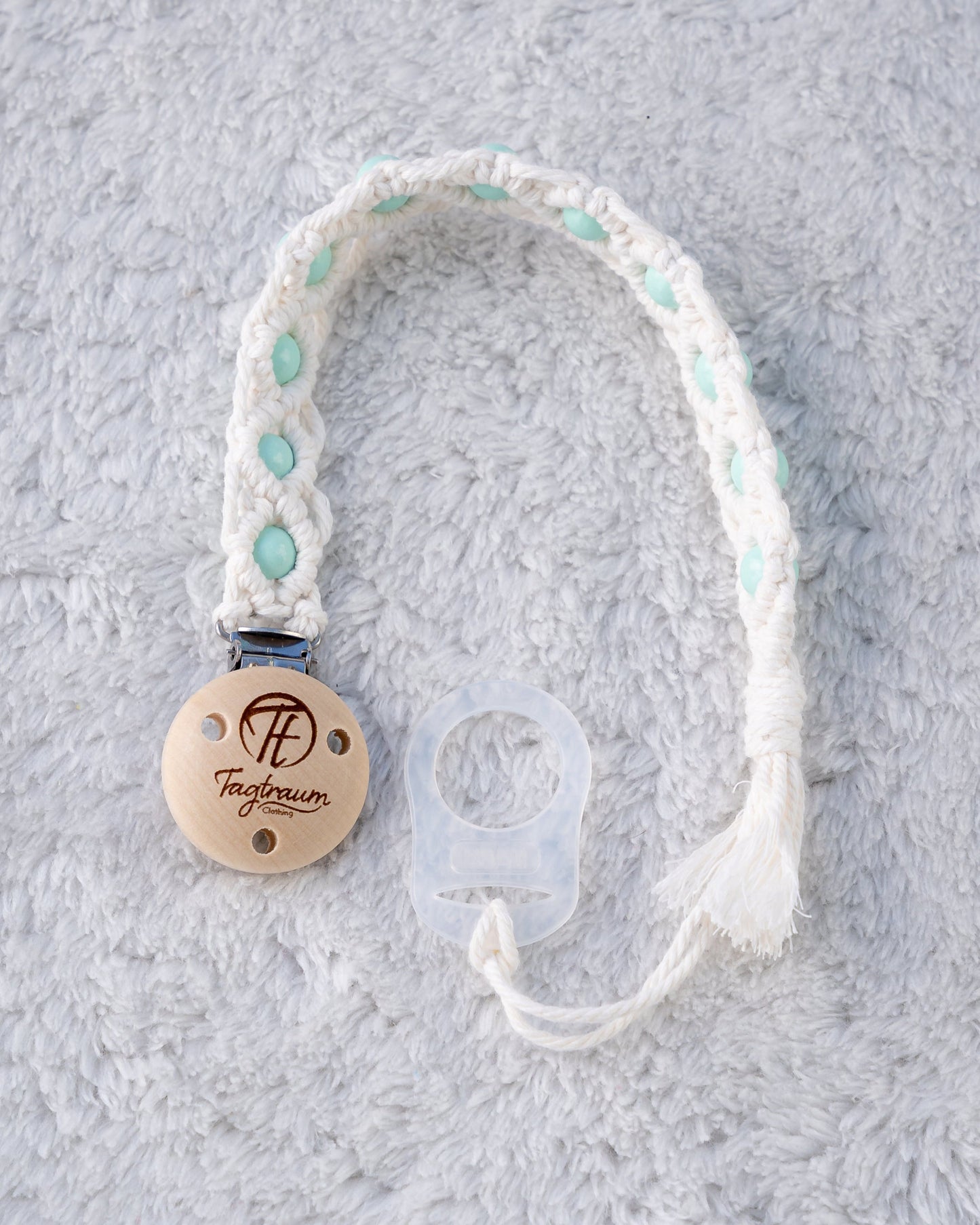 Schöne Schnullerkette aus weissem Garn mit türkisen Holzperlen, einem hochwertigen Schnullerclip aus Holz, und einem Adapter für MAM Schnuller. Auf dem Holzclip befindet sich eine dle Tagtraum Cothing Gravur mit Logo. Die Schnullerketten werden handgefertigt von Tagtraum Clothing in der Schweiz.