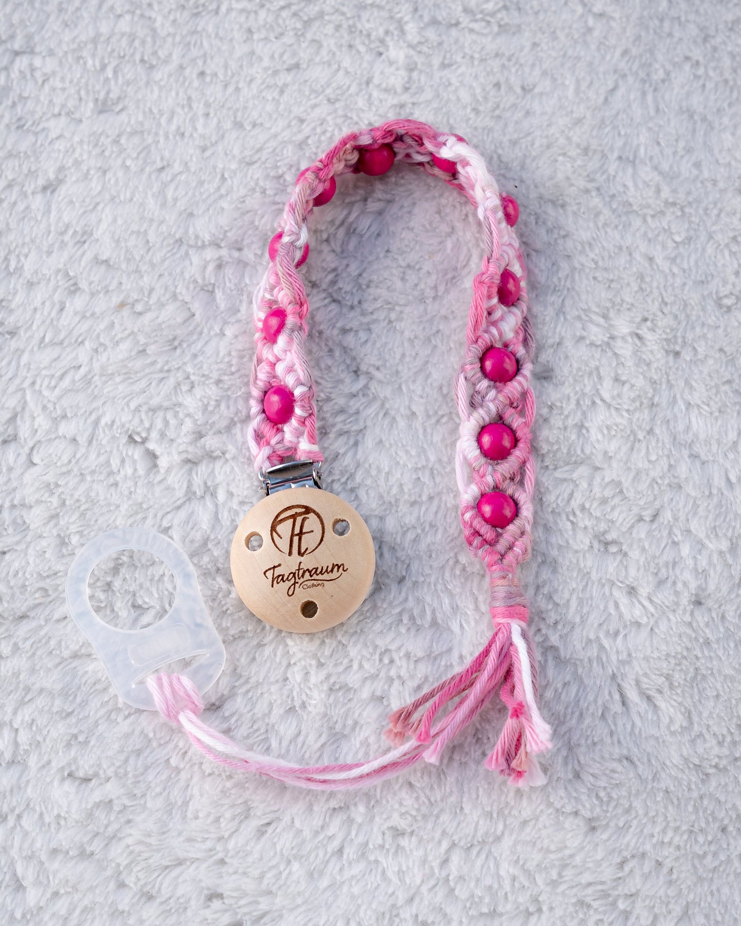 Schöne Schnullerkette aus rosa Garn mit pinken Holzperlen, einem hochwertigen Schnullerclip aus Holz, und einem Adapter für MAM Schnuller. Auf dem Holzclip befindet sich eine dle Tagtraum Cothing Gravur mit Logo. Die Schnullerketten werden handgefertigt von Tagtraum Clothing in der Schweiz.