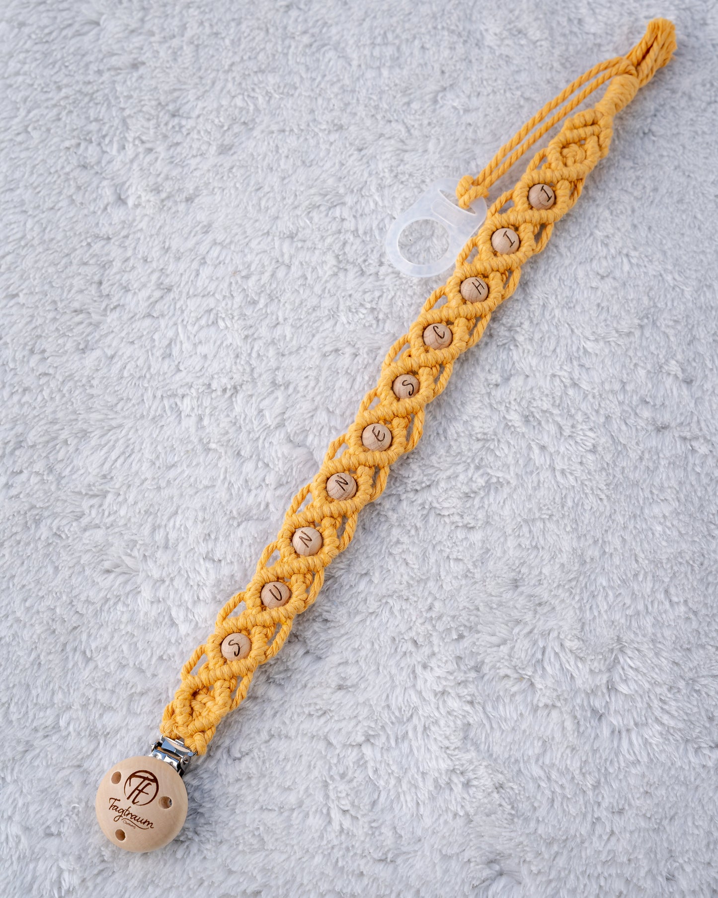Schöne Schnullerkette aus sonnengelbem Garn mit naturfarbenen Holzperlen mit Buchstaben "Sunneschii", einem hochwertigen Schnullerclip aus Holz, und einem Adapter für MAM Schnuller. Auf dem Holzclip befindet sich eine dle Tagtraum Cothing Gravur mit Logo. Die Schnullerketten werden handgefertigt von Tagtraum Clothing in der Schweiz.