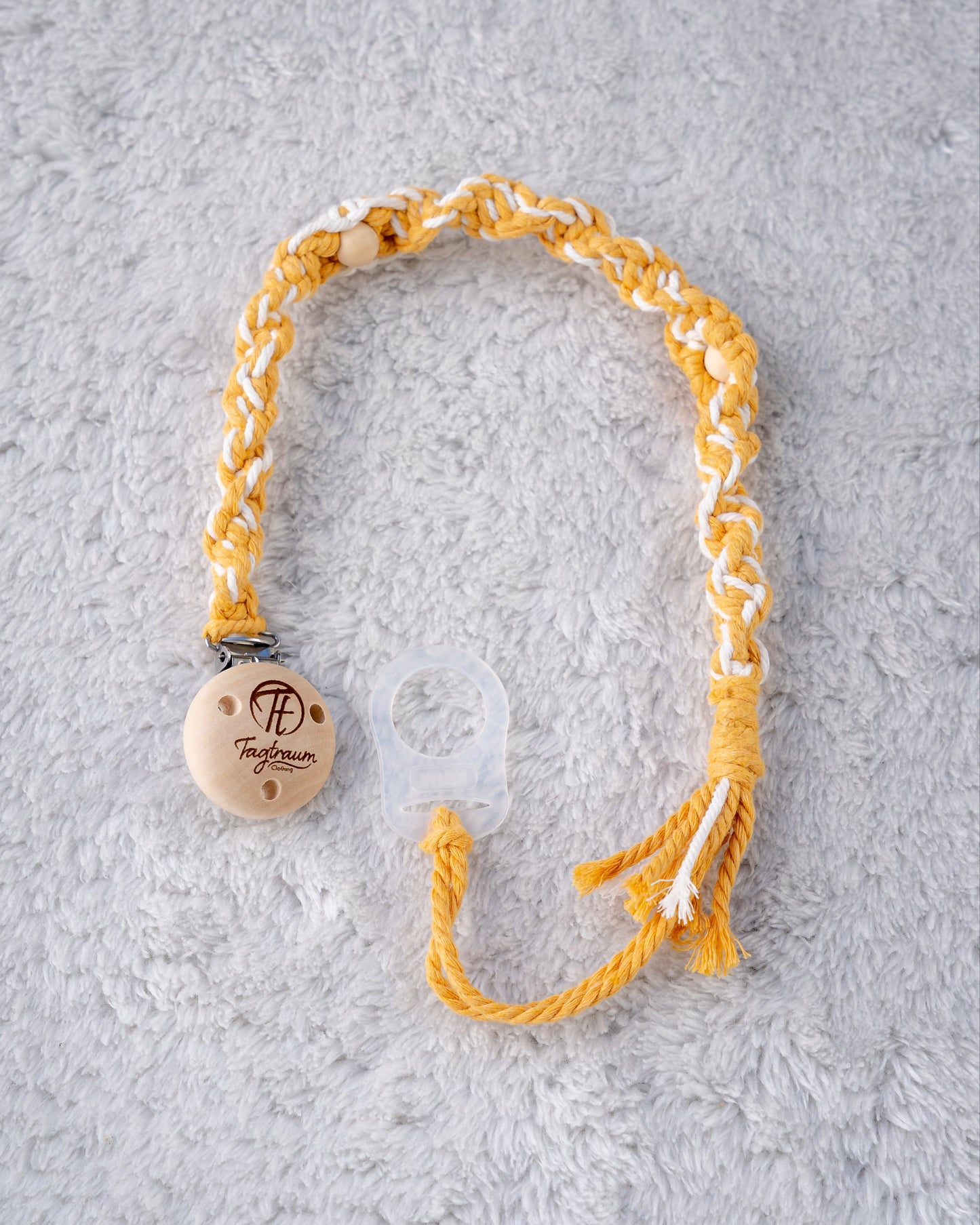 Schöne Schnullerkette aus sonnengelbem und weissem Garn mit natur Holzperlen, einem hochwertigen Schnullerclip aus Holz, und einem Adapter für MAM Schnuller. Auf dem Holzclip befindet sich eine dle Tagtraum Cothing Gravur mit Logo. Die Schnullerketten werden handgefertigt von Tagtraum Clothing in der Schweiz.