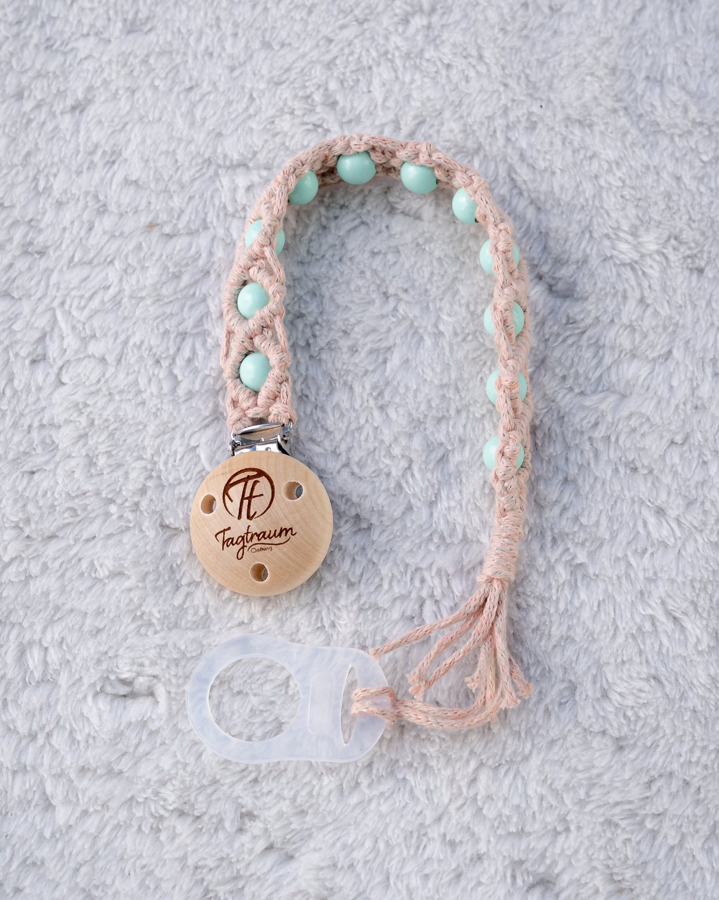 Schöne Schnullerkette aus lachsrosa Garn mit türkisen Holzperlen, einem hochwertigen Schnullerclip aus Holz, und einem Adapter für MAM Schnuller. Auf dem Holzclip befindet sich eine dle Tagtraum Cothing Gravur mit Logo. Die Schnullerketten werden handgefertigt von Tagtraum Clothing in der Schweiz.
