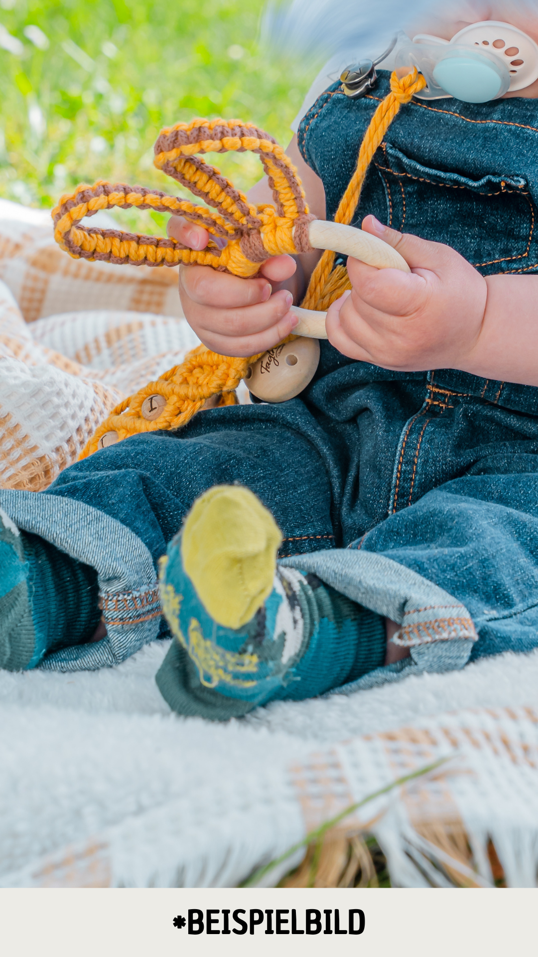Ein Baby hält einen süssen Hasenohren Beissring in der Hand und sitzt draussen auf einer Pick-Nick Decke, das Gesicht ist nicht zu sehen. Der Beissring ist aus nachhaltigen, umweltfreundlichen Materialien gefertigt und passt perfekt in kleine Baby-Hände. Zudem ist er aus natürlichen Materialien und komplett Schadstofffrei. Handgefertigt in der Schweiz.