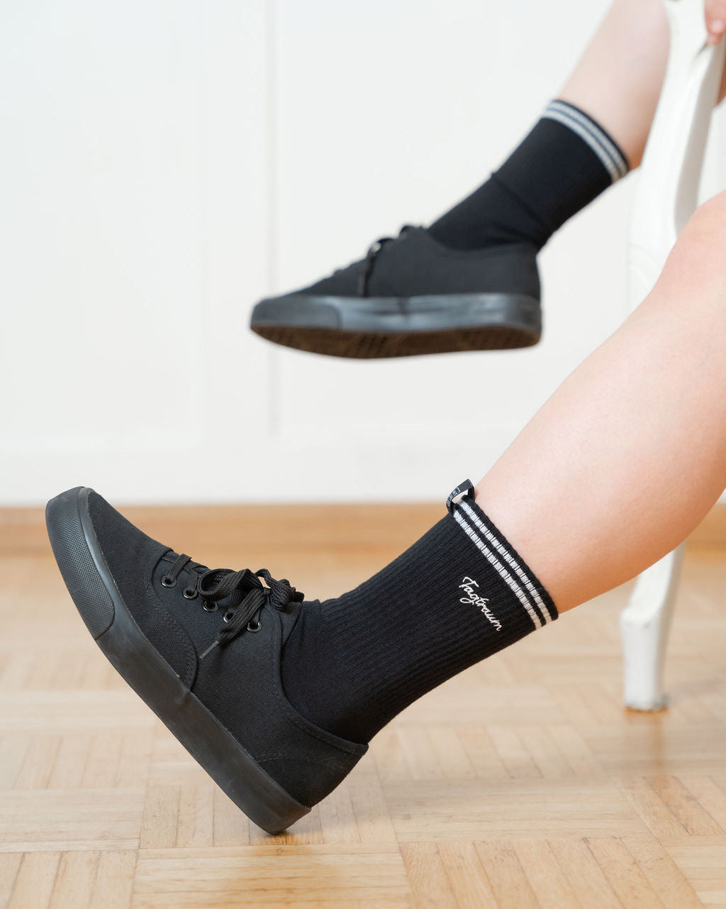 Schwarze Tennissocken mit zwei weissen Streifen und edlem Tagtraum Stick, getragen von einer Frau in schwarzen Sneaker