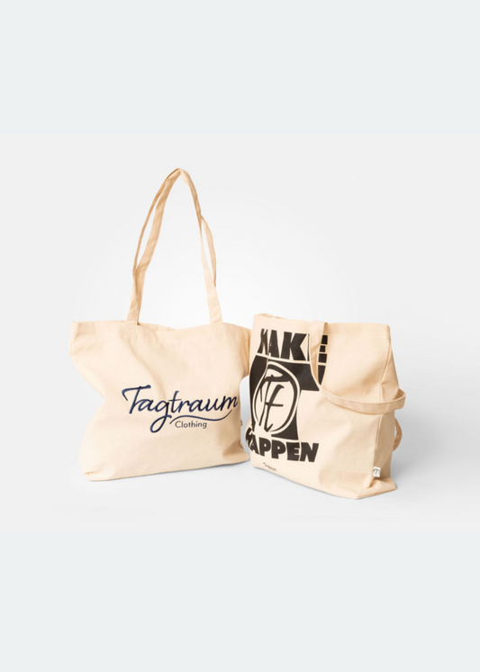 Zwei Shopper aus Bio-Baumwolle, einer mit einem schwarzen Make it Happen Print und der andere mit einem edlen, blauen Tagtraum Stick