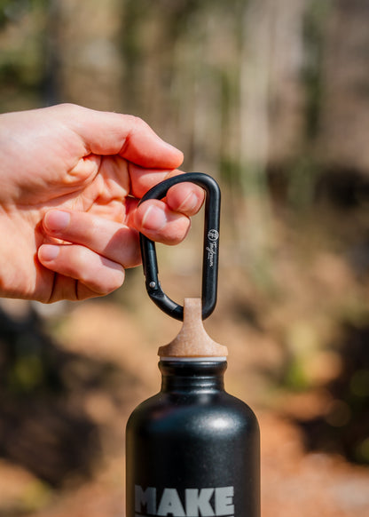 Ein kleiner, schwarzer Aluminium Karabiner, an dem eine Tagtraum Trinkflasche hängt