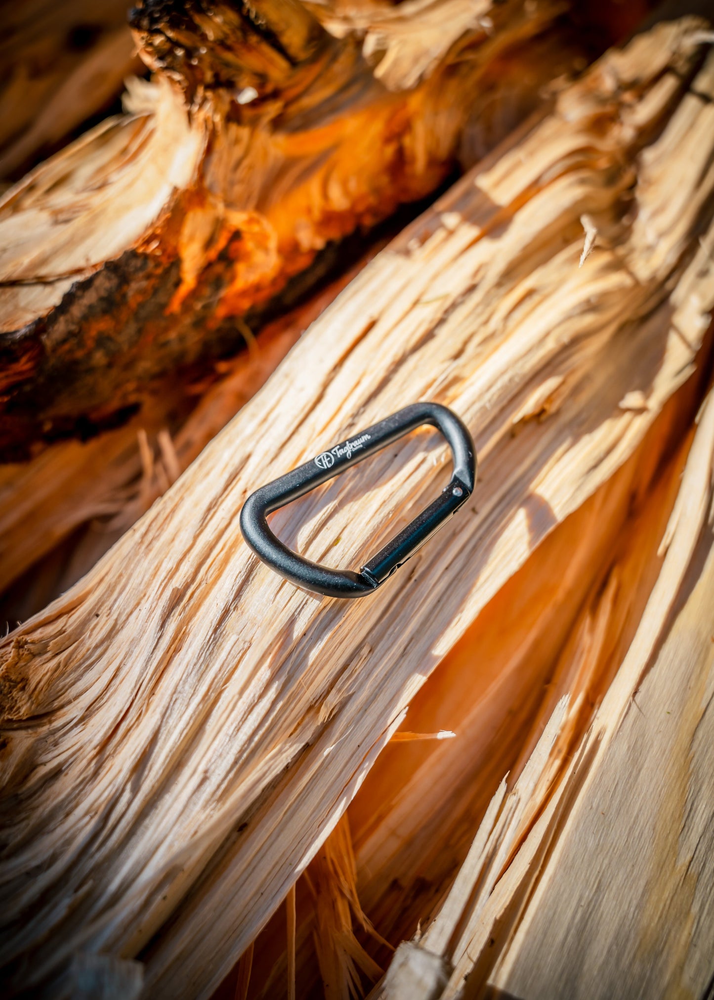 Ein kleiner, schwarzer Karabiner aus 100% Aluminium liegt auf einem Holzstapel