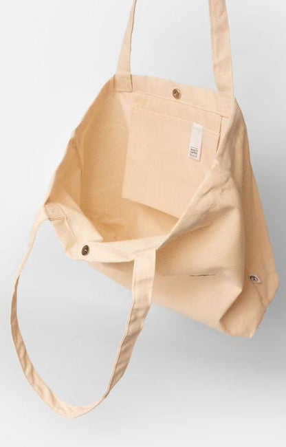 eine naturfarbene Bio-Baumwolltasche. Zu sehen ist die Innenseite des Shoppers, mit der praktischen Innentasche, der "Make it happen"-Lasche für den Schlüsselbund o.ä., sowie dem Druckknopf