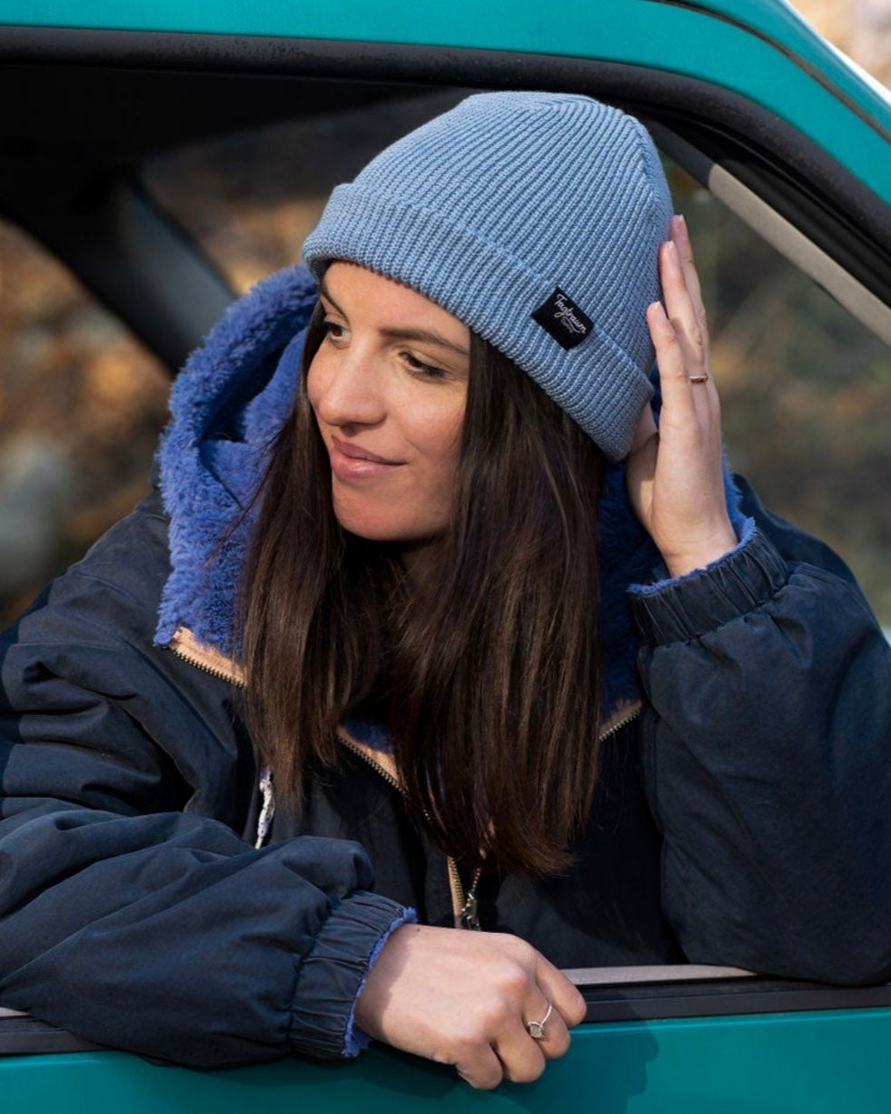 Ein weibliches Model trägt eine Winterjacke und ein Tagtraum Beanie in Graublau. Sie schaut aus dem offenen Fenster eines VW T4