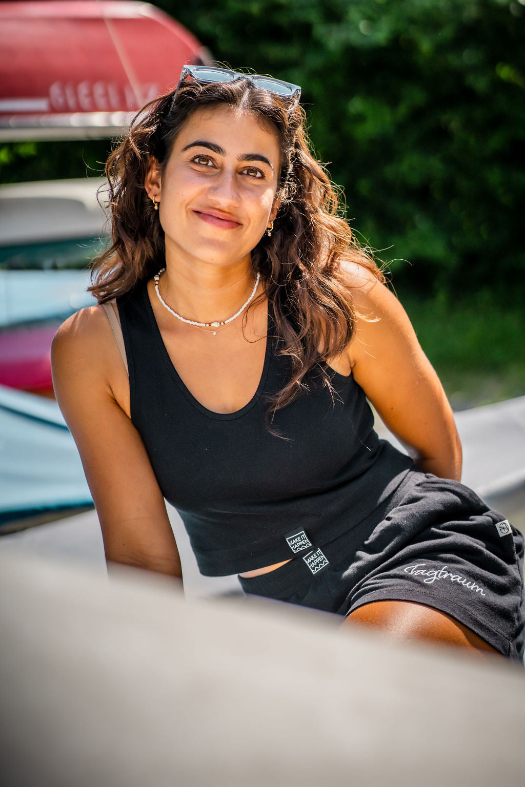 Eine junge Frau mit Sonnenbrille und Locken in einem schwarzen Tagtraum Crop Top und einer Shorts, beides aus 100% Bio-Baumwolle