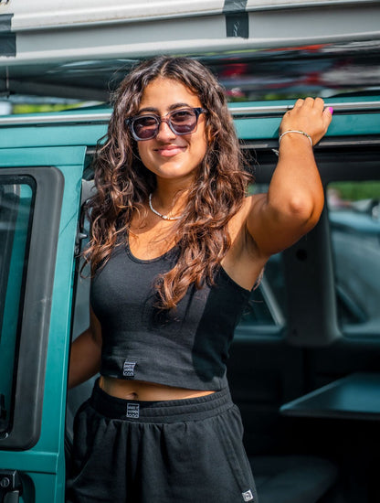 Eine junge Frau mit Sonnenbrille und Locken vor einen Van, mit einem schwarzen Tagtraum Crop Top und einer Shorts, beides aus 100% Bio-Baumwolle