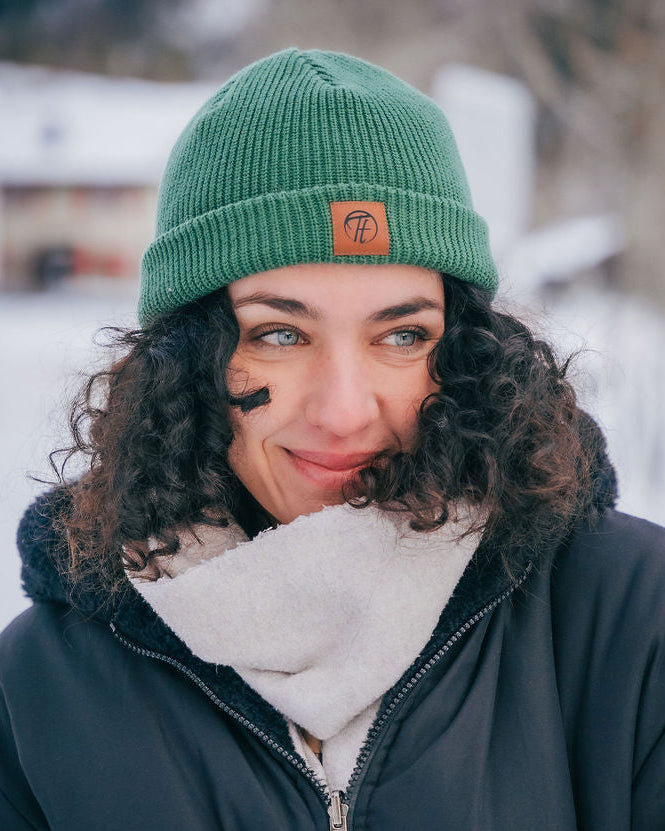 Ein Model, das natürlich lächelt und ein waldgrünes Fisherman Beanie trägt. Teil des Go Green Bundles. Fisherman Beanie aus 100% Bio-Baumwolle, fair hergestellt Polen.