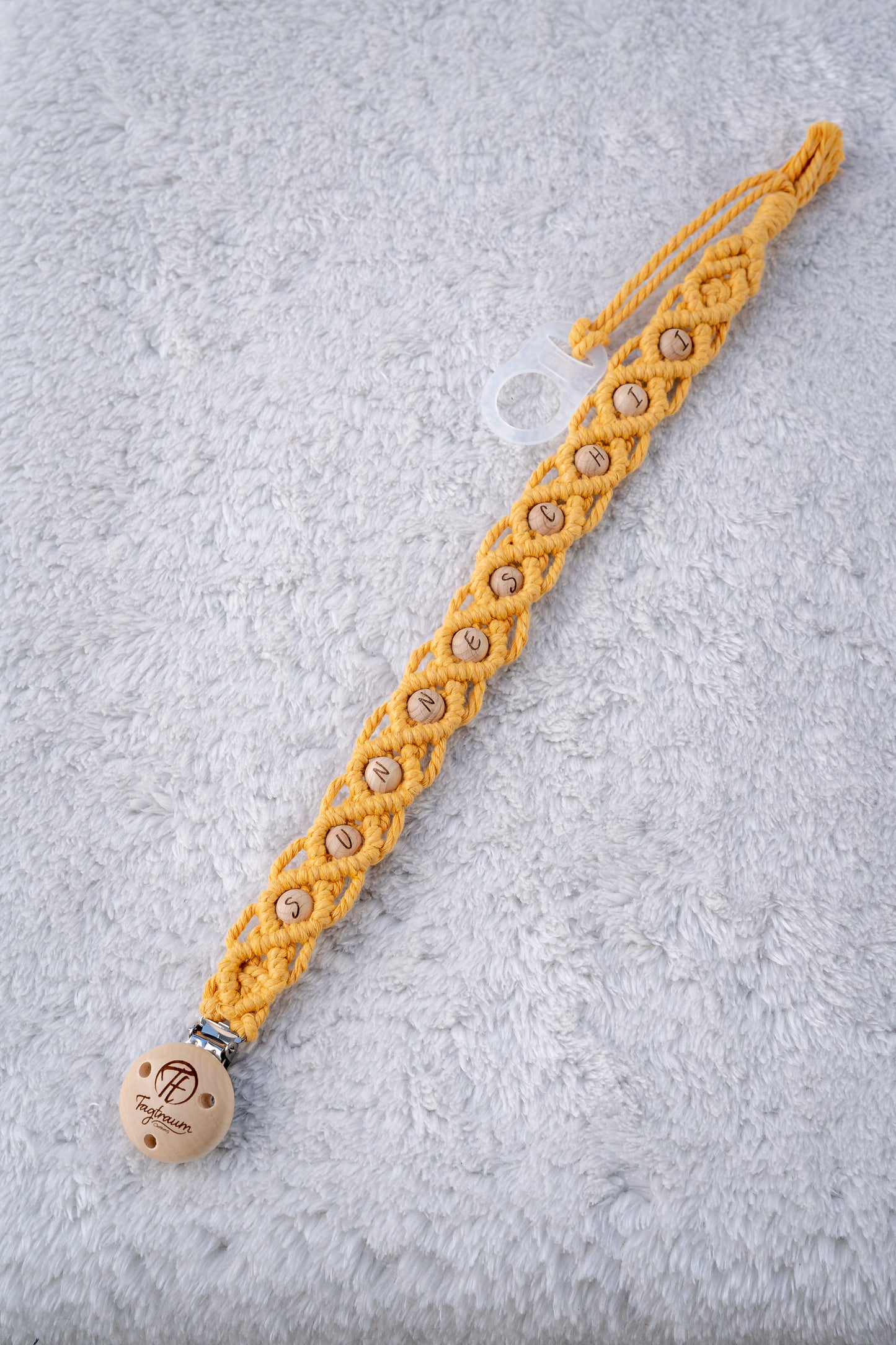 Schöne Schnullerkette aus sonnengelbem Garn mit naturfarbenen Holzperlen mit Buchstaben "Sunneschii", einem hochwertigen Schnullerclip aus Holz, und einem Adapter für MAM Schnuller. Auf dem Holzclip befindet sich eine dle Tagtraum Cothing Gravur mit Logo. Die Schnullerketten werden handgefertigt von Tagtraum Clothing in der Schweiz.