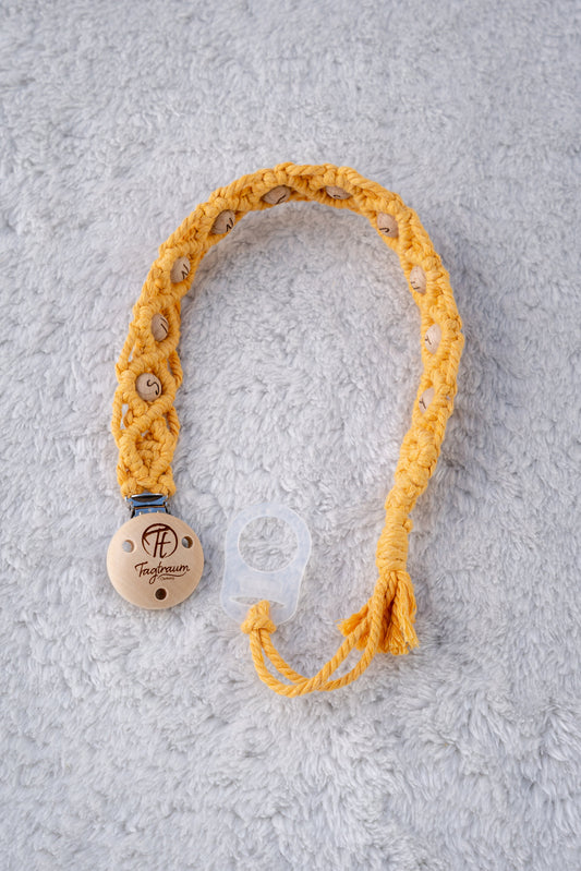 Schöne Schnullerkette aus sonnengelbem Garn mit naturfarbenen Holzperlen mit Buchstaben (Sunneschii), einem hochwertigen Schnullerclip aus Holz, und einem Adapter für MAM Schnuller. Auf dem Holzclip befindet sich eine dle Tagtraum Cothing Gravur mit Logo. Die Schnullerketten werden handgefertigt von Tagtraum Clothing in der Schweiz.