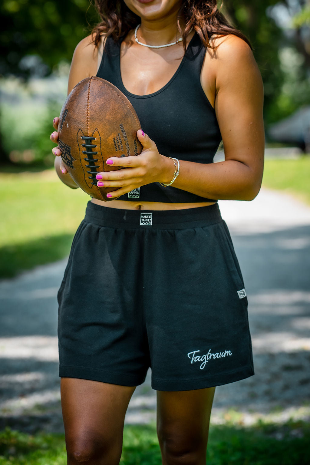 Bio Baumwolle Shorts in Schwarz, getragen von einer Frau, die sich draussen in der Natur befindet, in den Händen hält sie einen Football. Die Shorts trägt sie in Kombination mit einem schwarzen Tagtraum Crop Top