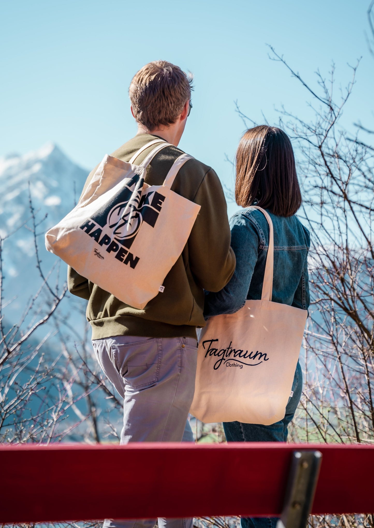 Zwei Bio-Baumwoll Shopper, getragen von einem Pärchen, welches draussen vor einer Bank steht und in die Berge schaut