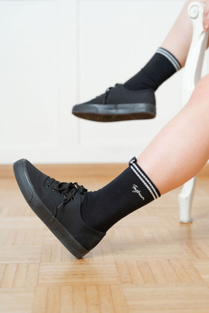 Schwarze Tennissocken mit zwei weissen Streifen und edlem Tagtraum Stick, getragen von einer Frau in schwarzen Sneaker