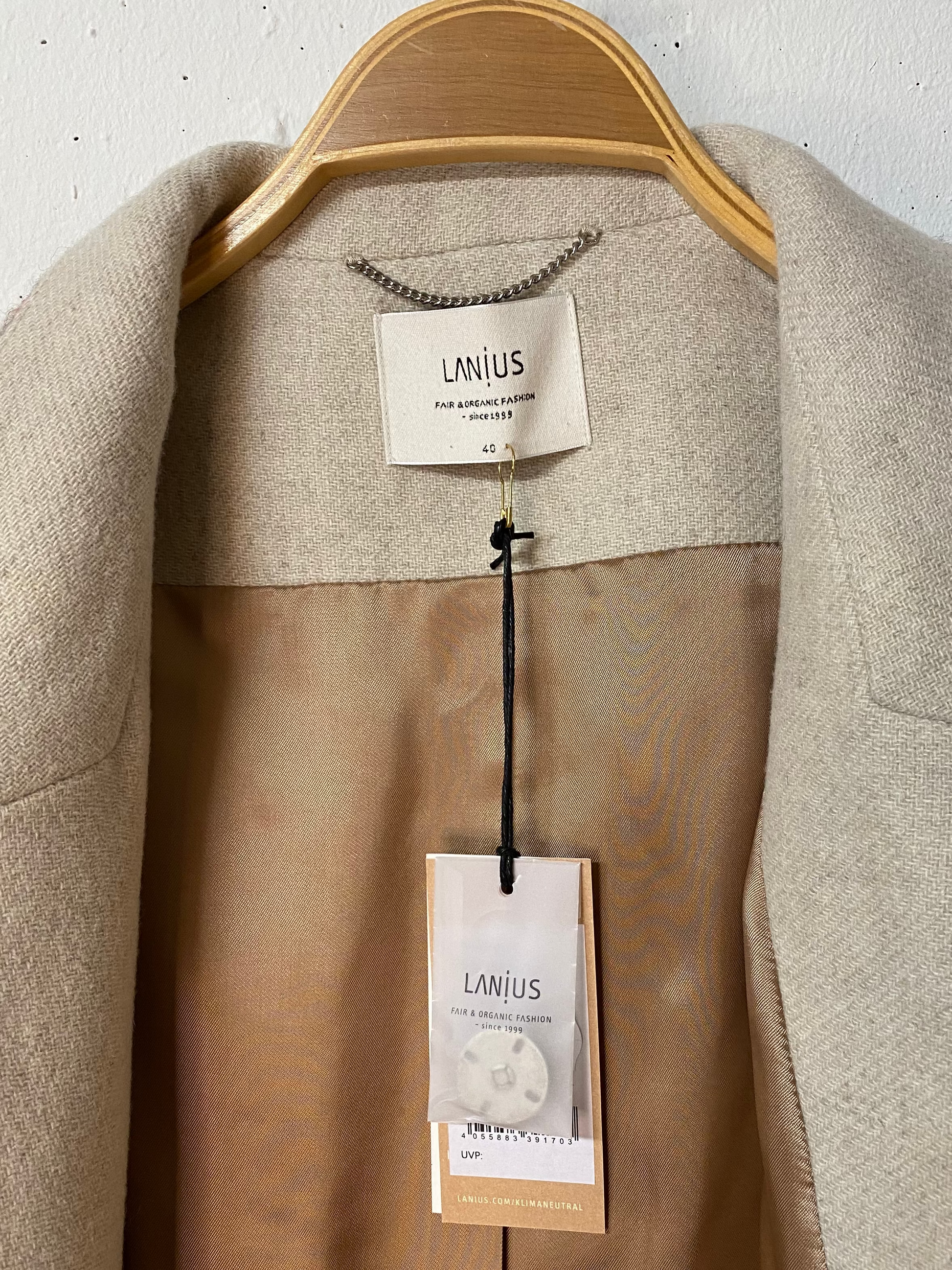 Innenseite eines schönen, kuschelig warmen Wollmantel von Lanius. Man sieht den Hang Tag mit Ersatzknopf, sowie das Label, die Aufhängelasche und die Grössenangabe. 